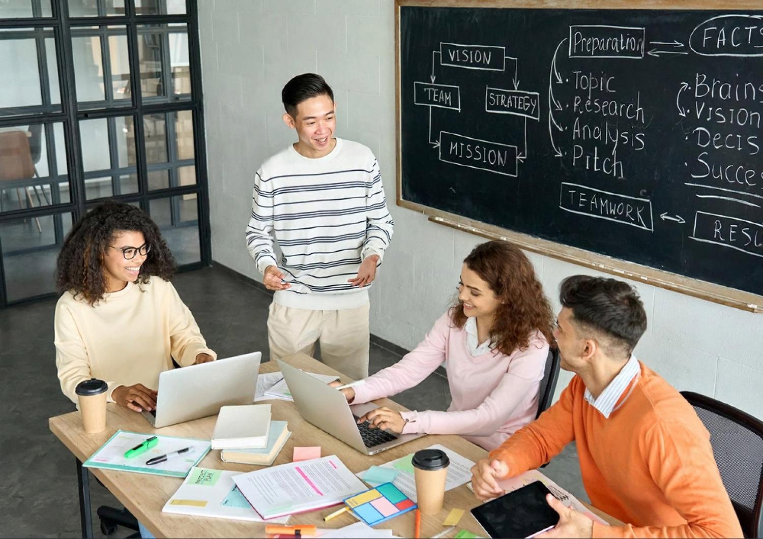 Students collaborating on a group project with laptops in front of a strategy board, preparing for university applications